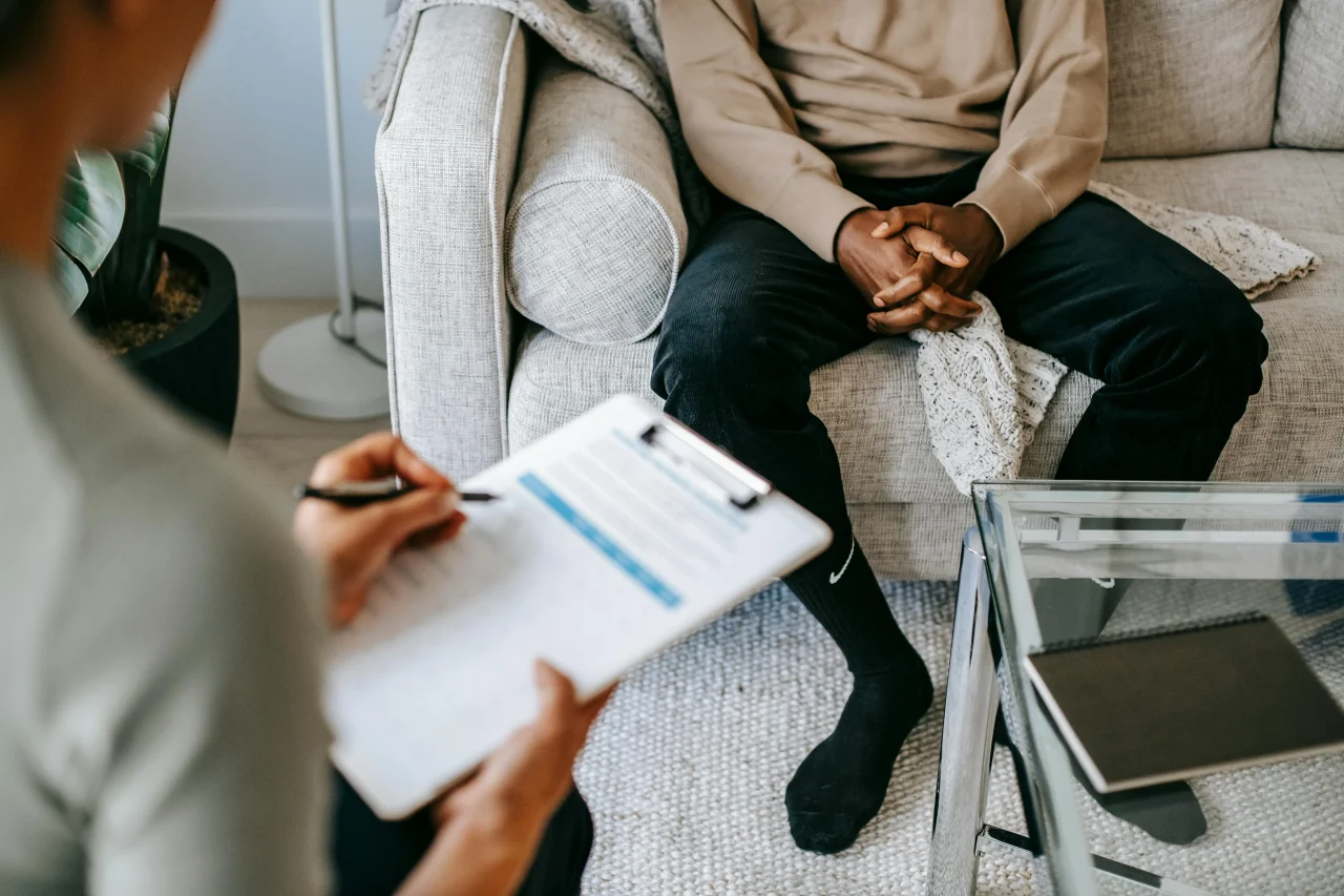 Akzeptanz- und Commitmenttherapie 4 Therapeutin schreibt auf ihrem Klemmbrett, Patient sitzt vor ihr auf einer Couch