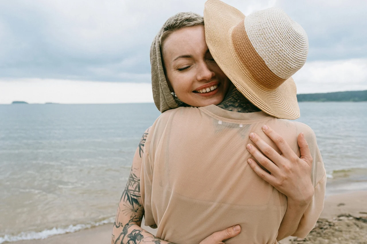 Wie sich Meditation auf dein Liebesleben auswirkt 2 Zwei Frauen umarmen sich dankbar am Strand – emotionaler Moment im Liebesleben