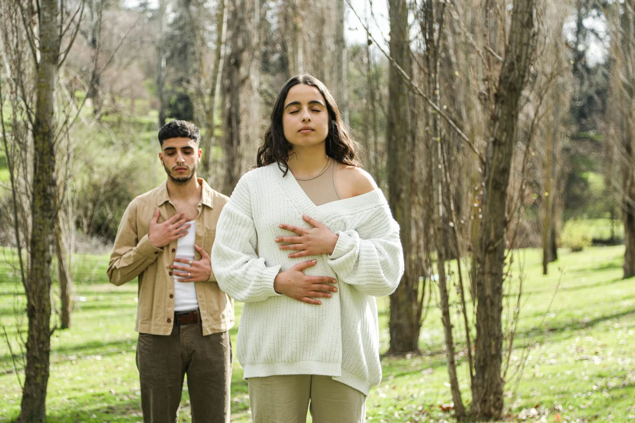 Wie sich Meditation auf dein Liebesleben auswirkt 3 Mann und Frau meditieren im Park mit den Händen auf Bauch und Brust
