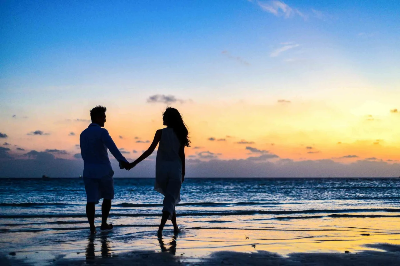Wie sich Meditation auf dein Liebesleben auswirkt 1 Ein Paar spaziert am Strand Hand in Hand bei Sonnenuntergang