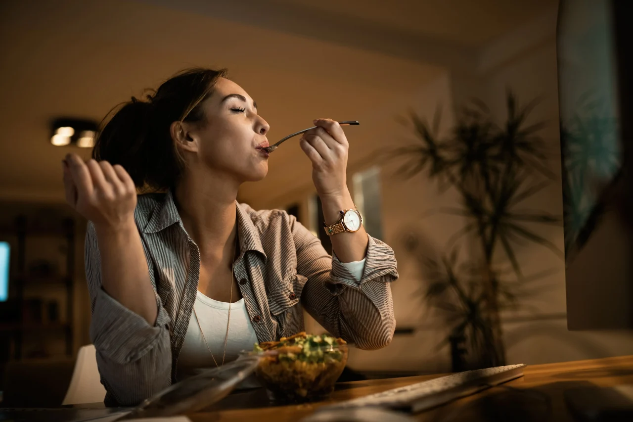 low angle view young woman eating salad with her eyes closed while using computer night home 1