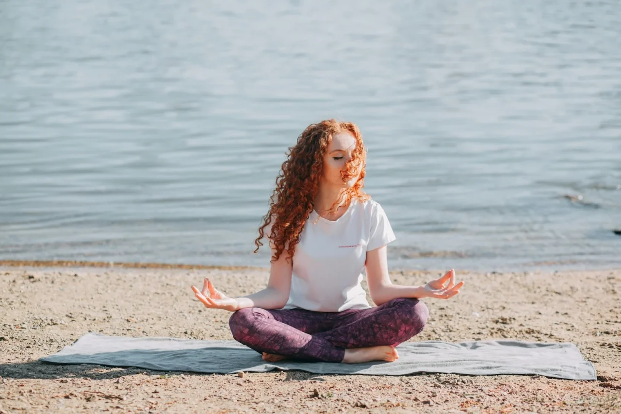 10 Fragen an Katrin unsere Meditationslehrerin 3 Frau meditiert am Wasser auf einem Handtuch in Schneidersitz