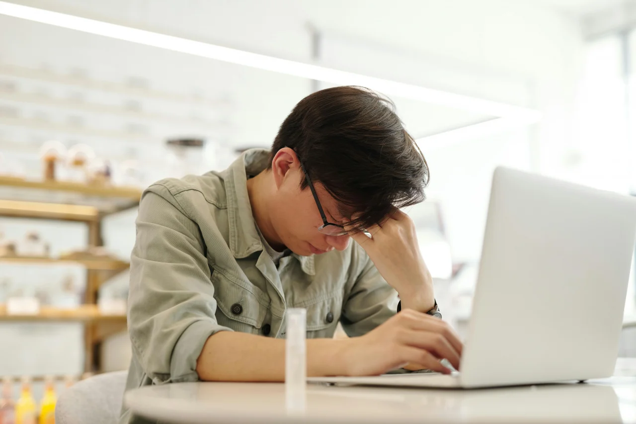 Psychische Belastungen am Arbeitsplatz 1 Mann sitzt am Laptop und greif sich belastend an den Kopf aufgrund von psychische Belastungen am Arbeitsplatz
